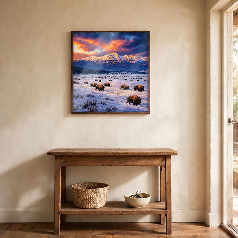 Square bison wall art framed above a wooden console table in a rustic entryway, winter buffalo herd and snow-capped mountains poster