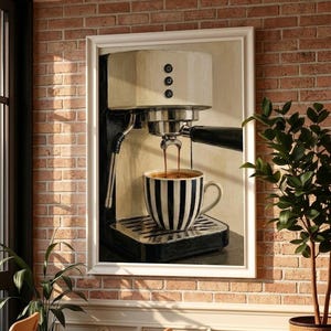 May include: A framed wall art print depicting a cream and black espresso machine brewing coffee into a black and white striped ceramic mug. The machine features a silver portafilter, a steam wand, and three circular control buttons on the front.