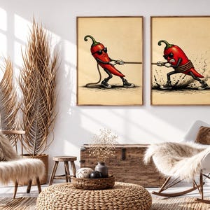 May include: Two framed wall art prints featuring a cartoon red chilli pepper wearing sunglasses and black trainers. In the left print, the chilli pulls a rope, and in the right print, the chilli is tied with a rope, creating a tug-of-war scene.