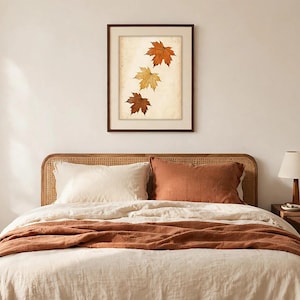 May include: A framed wall art print featuring three autumn maple leaves in shades of orange, yellow, and brown arranged vertically against a textured, off-white background. The artwork is enclosed in a simple, dark brown wooden frame.