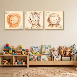 K&ouml;nnte beinhalten: Drei quadratische Wandbilder mit Aquarellillustrationen eines L&ouml;wen, eines Zebras und eines Affen. Jedes Tier ist vor einem hellen Hintergrund mit kleinen gr&uuml;nen Blattakzenten dargestellt, in hellem Holz gerahmt und &uuml;ber einem Spielzeugregal.