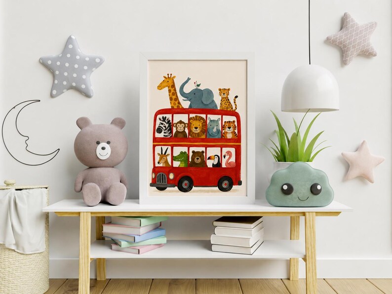 May include: A framed art print featuring a bright red double-decker bus filled with various illustrated animals, including a giraffe, elephant, lion, zebra, and monkey, displayed in a white frame on a wooden table with books and toys.