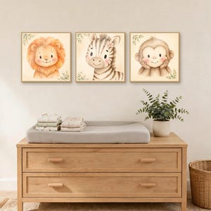 K&ouml;nnte beinhalten: Drei quadratische Wandbilder mit Aquarellillustrationen eines L&ouml;wen, eines Zebras und eines Affen. Jedes Tier ist mit weichen Z&uuml;gen dargestellt und von kleinen gr&uuml;nen Blattakzenten auf einem hellen cremefarbenen Hintergrund umgeben.