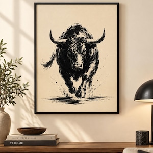 K&ouml;nnte beinhalten: Ein gerahmter Kunstdruck mit einer schwarzen Tuschezeichnung eines st&uuml;rmenden Stiers auf hellbeigem Hintergrund. Das Kunstwerk zeigt den Stier in einer dynamischen Vorw&auml;rtsbewegung mit sichtbaren Pinselstrichstrukturen und schwarzen Farbspritzern.