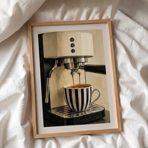May include: A framed art print depicting a cream and black espresso machine brewing coffee into a black and white striped ceramic mug. The machine features three circular buttons on the front panel and a metallic drip tray base.