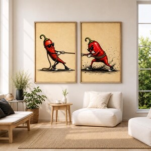 May include: Two framed wall art prints featuring a cartoon red chilli pepper character wearing sunglasses and trainers, engaged in a tug-of-war match. The illustrations are set against a textured, light tan background with visible ink details.