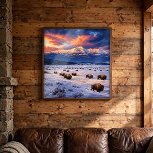 Bison wall art in a dark wood square frame above a leather sofa in a rustic lodge living room, winter buffalo herd and snowy mountain sunset print