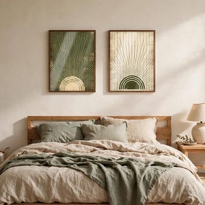 May include: Two rectangular wall art prints in dark wood frames hanging above a bed. The left print features a green background with a gold sunburst design. The right print features a cream background with a dark green sunburst design.