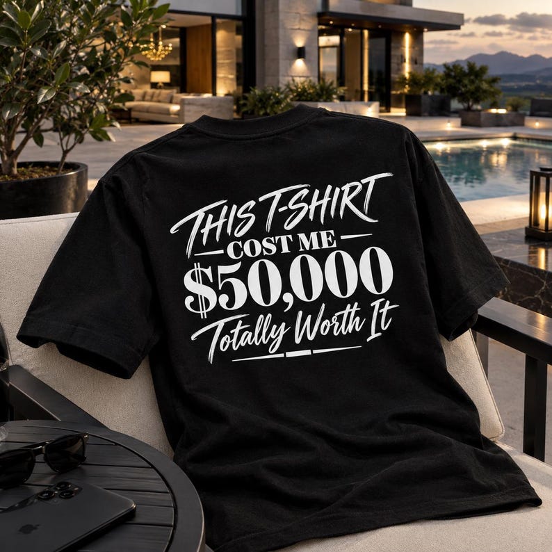 May include: A black short-sleeved t-shirt featuring white screen-printed text on the back that reads: THIS T-SHIRT COST ME $50,000 Totally Worth It. The shirt has a crew neckline and is made of a solid black fabric with bold white lettering.
