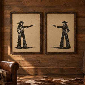K&ouml;nnte beinhalten: Zwei gerahmte Wandbilder mit schwarzen Tuschezeichnungen einer Cowgirl-Figur mit breitkrempigem Hut und Fransenhose, die eine Pistole h&auml;lt. Das Kunstwerk ist auf beigefarbenem Hintergrund und in dunkle Holzrahmen gefasst.