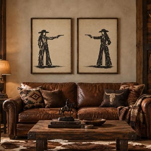 K&ouml;nnte beinhalten: Zwei gerahmte Wandbilder mit schwarzen Tuschezeichnungen von Figuren mit Cowboyh&uuml;ten und Fransenhosen, die Pistolen halten, nebeneinander an einer Wand &uuml;ber einem braunen Ledersofa mit gemusterten Kissen und einem Couchtisch aus Holz.