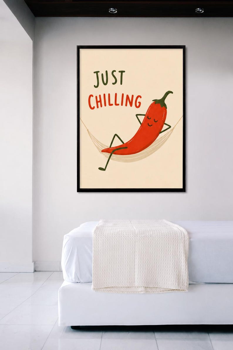May include: A framed wall art print featuring a cartoon red chili pepper with a smiling face relaxing in a beige hammock. The text "JUST CHILLING" is printed in dark green and red letters above the chili pepper on a light cream background.