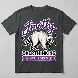 May include: A charcoal grey short-sleeve t-shirt featuring a graphic of a white raccoon with black markings. The text reads "Jimothy" in purple, "OVERTHINKING" in black, and "SINCE FOREVER" in white on a purple banner, accented by four-pointed stars.