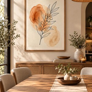 May include: A framed wall art print featuring a black line drawing of an olive branch layered over two soft, circular watercolor washes in shades of burnt orange and light tan on a cream-colored background, displayed in a wooden frame.