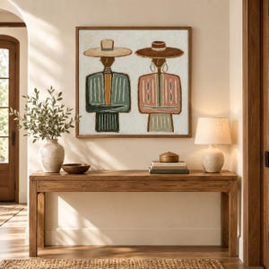 May include: A square framed wall art piece depicting two stylized figures wearing wide-brimmed hats. The left figure wears a blue and mustard striped garment, while the right figure wears a pink and green striped garment. Both have simple line-drawn features.