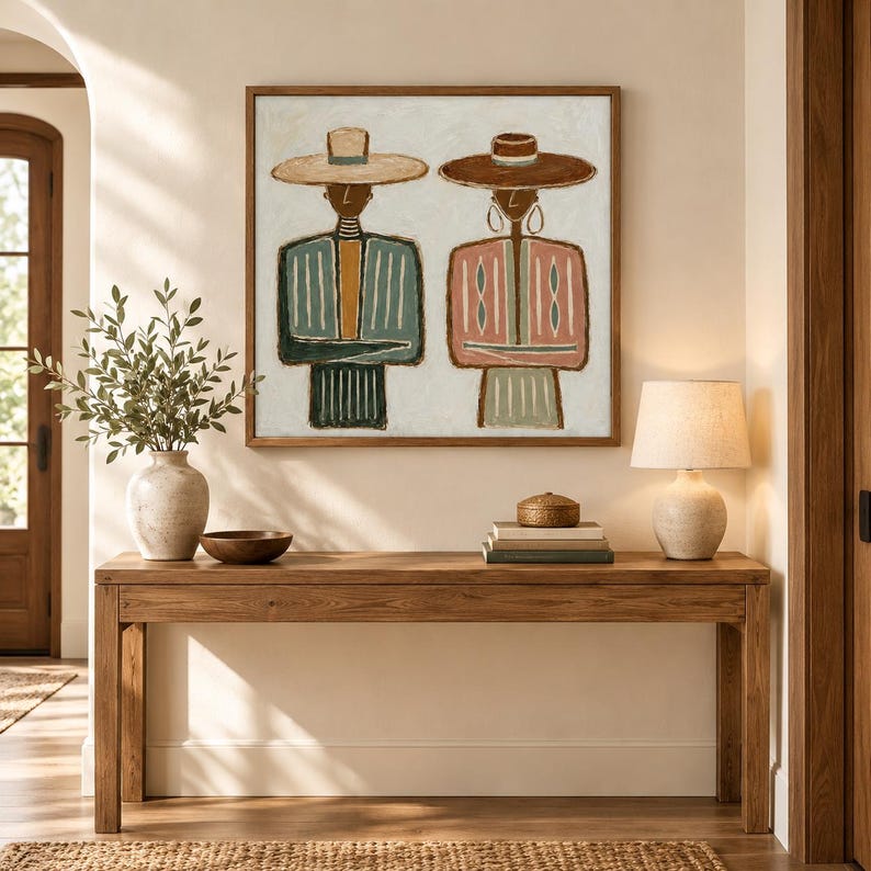 May include: A square framed wall art piece depicting two stylized figures wearing wide-brimmed hats. The left figure wears a blue and mustard striped garment, while the right figure wears a pink and green striped garment. Both have simple line-drawn features.