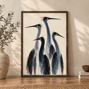 May include: A framed wall art print featuring a watercolour illustration of four blue herons with long necks and sharp beaks. The birds are rendered in shades of dark blue, grey, and black against a cream-coloured background, set in a dark wood frame.