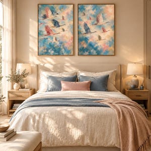 May include: Two rectangular framed wall art pieces featuring oil-style paintings of birds in flight against a soft, cloudy sky with blue, pink, and white hues. The artwork is displayed symmetrically above a bed with neutral bedding and pillows.