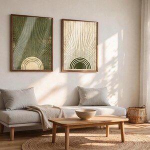 May include: Two framed rectangular wall art prints featuring a sunburst motif. The left print has a dark green background with a gold sun, while the right print has a cream background with a dark green sun. Both feature radiating lines.
