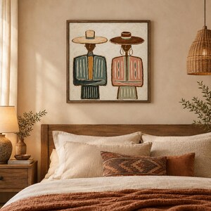 May include: A square framed wall art piece featuring a stylized illustration of two figures wearing wide-brimmed hats. The figure on the left wears a blue and yellow striped garment, while the figure on the right wears a pink and white patterned top.