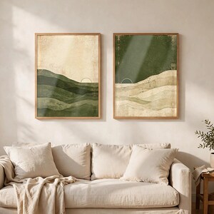 May include: Two rectangular framed wall art prints featuring abstract landscape designs. The left print displays layered green hills against a cream sky, while the right print shows layered cream hills against a dark green sky, both with a thin sun arc.