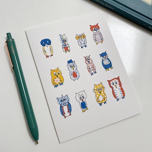 以下が含まれることがあります： 白いカードに、カラフルなフクロウのイラストが12個描かれています。フクロウは漫画のようなスタイルで描かれており、それぞれ異なる模様やアクセサリーを身につけています。フクロウはすべて正面を向いており、大きく丸い目を持っています。