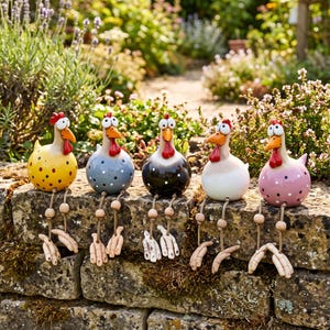 Könnte beinhalten: Fünf Keramik-Hühnerfiguren mit runden Körpern, orangefarbenen Schnäbeln und roten Kämmen. Jedes Huhn hat baumelnde Beine mit Holzperlen und Füßen. Die Hühner sind gelb, hellblau, schwarz, weiß und rosa gefärbt und mit Punkten versehen.