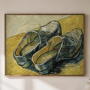 May include: A framed wall art print depicting an oil painting of a pair of worn, dark-toned leather clogs resting on a textured, golden-yellow surface. The artwork features visible brushstrokes and a high-contrast colour palette of deep blues, greys, and vibrant yellows.