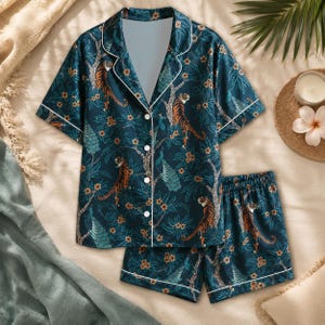May include: A dark teal pajama set featuring a short-sleeved button-down shirt and matching shorts. The fabric displays a repeating pattern of orange tigers, blue peacocks, and small flowers set against a backdrop of dark green leafy branches.