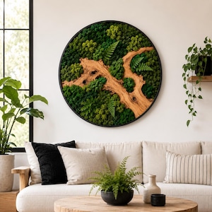 May include: A circular wall art piece featuring a black frame filled with preserved green moss, various small ferns, and a central piece of light brown driftwood. The arrangement creates a textured, forest-like landscape within the round frame.