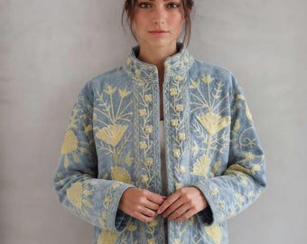 May include: A light blue jacket featuring a high collar and long sleeves, adorned with intricate yellow floral embroidery throughout the front and sleeves. The garment has a straight hemline and a button-down front closure with matching fabric buttons.