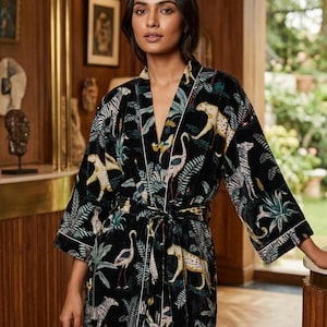 May include: A black velvet robe featuring a vibrant jungle-inspired print with illustrations of leopards, zebras, and flamingos amidst tropical foliage. The garment includes a matching tie belt at the waist and white piping along the lapels and cuffs.