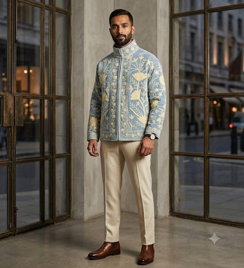 May include: A light blue quilted jacket featuring a high collar, a full-length front zipper, and cream-colored floral embroidery. The jacket is paired with cream-colored trousers and brown leather boots, creating a coordinated ensemble.