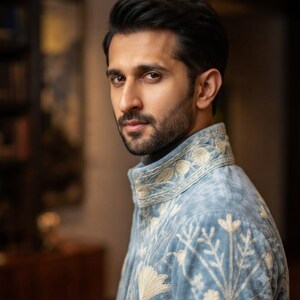 May include: A light blue jacket featuring intricate cream-colored floral embroidery on the high collar and shoulders. The garment is crafted from a soft, textured fabric and displays detailed botanical patterns across the chest and sleeve area.