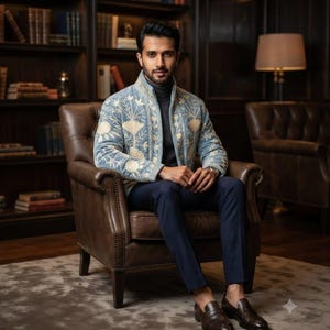 May include: A light blue zip-up jacket featuring cream-colored floral embroidery, worn over a dark gray turtleneck sweater. The outfit is completed with dark navy blue trousers and dark brown leather loafers, creating a cohesive ensemble.