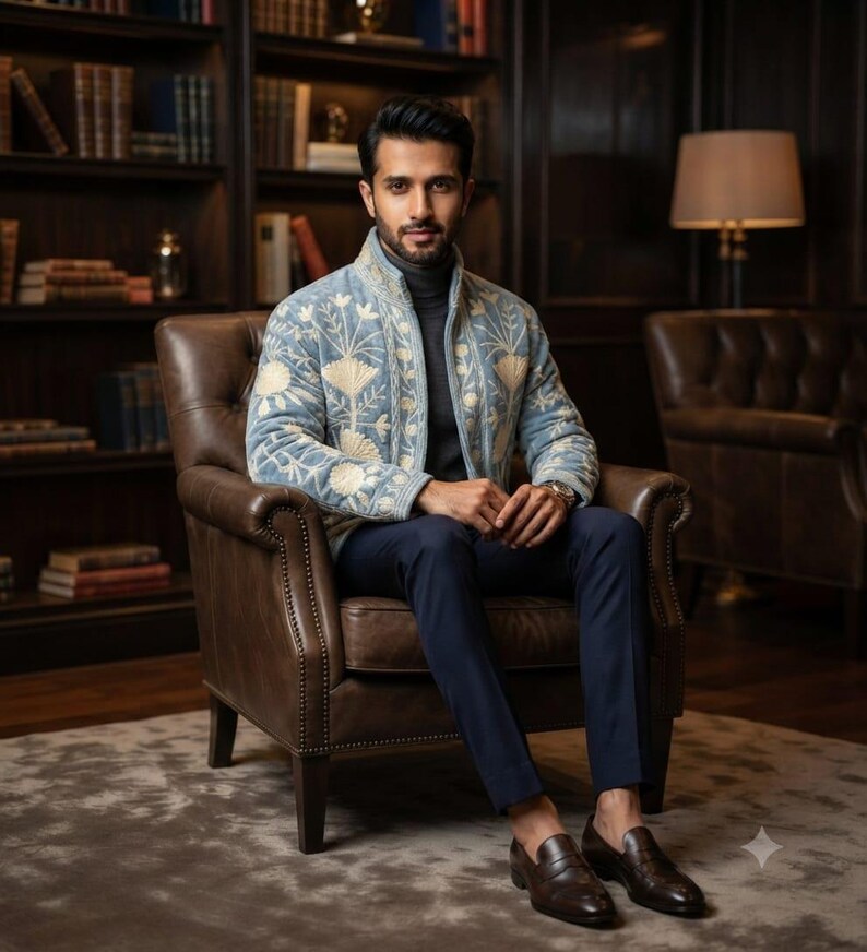 May include: A light blue zip-up jacket featuring cream-colored floral embroidery, worn over a dark gray turtleneck sweater. The outfit is completed with dark navy blue trousers and dark brown leather loafers, creating a cohesive ensemble.