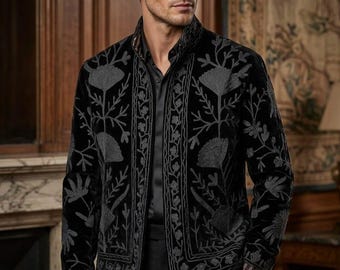 May include: A black velvet jacket featuring a high collar and long sleeves, adorned with intricate gray floral embroidery along the front panels and cuffs. The garment is worn over a black button-down shirt and black trousers, creating a cohesive look.