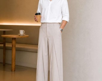May include: A crisp white long-sleeved button-down shirt paired with high-waisted beige wide-leg trousers featuring prominent vertical pleats. The outfit is completed with black leather loafers and a silver wristwatch on the left wrist.