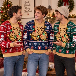 May include: Three long-sleeve knit jumpers in red, blue, and green, each featuring a tan chest panel with a graphic of two cookies and string lights. The jumpers display patterns of snowmen, snowflakes, candy canes, and gift boxes.