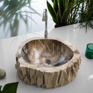Könnte beinhalten: Ein rundes Aufsatzwaschbecken aus versteinertem Holz mit einer natürlichen, rau strukturierten Rindenaußenseite und einem polierten, glatten Innenbereich mit braunen und beigefarbenen Marmormustern. Ein hoher, verchromter Wasserhahn steht dahinter.