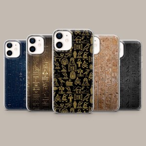 May include: Five smartphone cases arranged in a row, each featuring ancient Egyptian-themed designs. The cases display various patterns including golden hieroglyphics, stylized icons of pharaohs, deities, camels, and palm trees on dark and textured backgrounds.