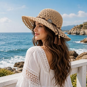 May include: A tan crocheted sun hat featuring a wide brim with an openwork pattern. The hat is adorned with a dark brown cord band, wooden beads, a silver-toned circular metal emblem with a floral design, and two hanging brown tassels.