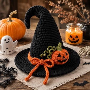 May include: A black crocheted witch hat featuring a pointed, slightly curved top. The hat is decorated with an orange crocheted bow and a small, orange crocheted jack-o'-lantern with green curly vines attached to the base of the crown.