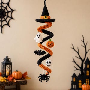May include: A hanging crochet decoration featuring a black witch hat at the top, followed by a spiral of orange and black yarn. Attached to the spiral are small crocheted figures including a white ghost, orange pumpkin, black bat, white skull, and black spider.