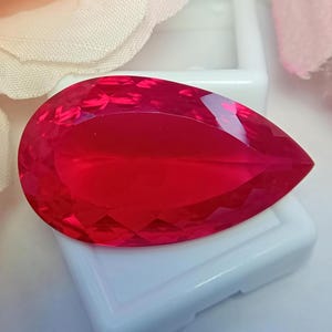 May include: A vibrant, pear-shaped loose gemstone with a deep red colour and a faceted surface. The stone features a pointed end and a rounded base, reflecting light across its polished, geometric cut facets to create a brilliant, clear appearance.