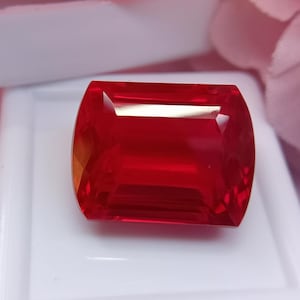Peut inclure: Une pierre précieuse rectangulaire d'un rouge profond avec des surfaces facettées qui reflètent la lumière. La pierre présente des bords nets et une finition polie, affichant une teinte cramoisie intense et uniforme dans tout son corps transparent.