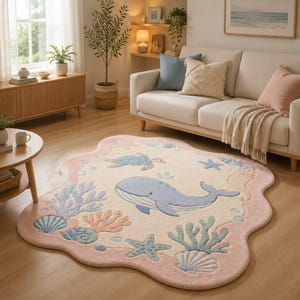 Puede incluir: Una alfombra de forma irregular similar a una nube con un centro color crema, decorada con una ballena azul claro, una tortuga marina y varios motivos marinos como corales, estrellas de mar y conchas en tonos pastel, con un borde rosa suave.
