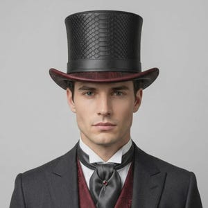 May include: A black top hat with a snakeskin-textured crown and a dark red brim. The hat is worn with a white collared shirt, a dark grey cravat featuring a small red gemstone pin, a dark red patterned vest, and a charcoal grey suit jacket.