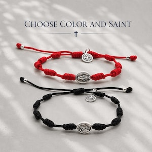 Könnte beinhalten: Zwei verstellbare Kordelarmbänder, eines in Rot und eines in Schwarz, jeweils mit einer Reihe von Knoten, einer zentralen ovalen silberfarbenen religiösen Medaille und einem kleinen runden silberfarbenen Anhänger. Der Text CHOOSE COLOR AND SAINT steht darüber.