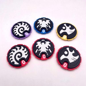 May include: Six circular game tokens featuring black and white graphic designs. Two tokens have a spiral pattern, two have a bird-like emblem, and two have a jagged wing motif. Each token has a colored border and a small tab with the number 0.